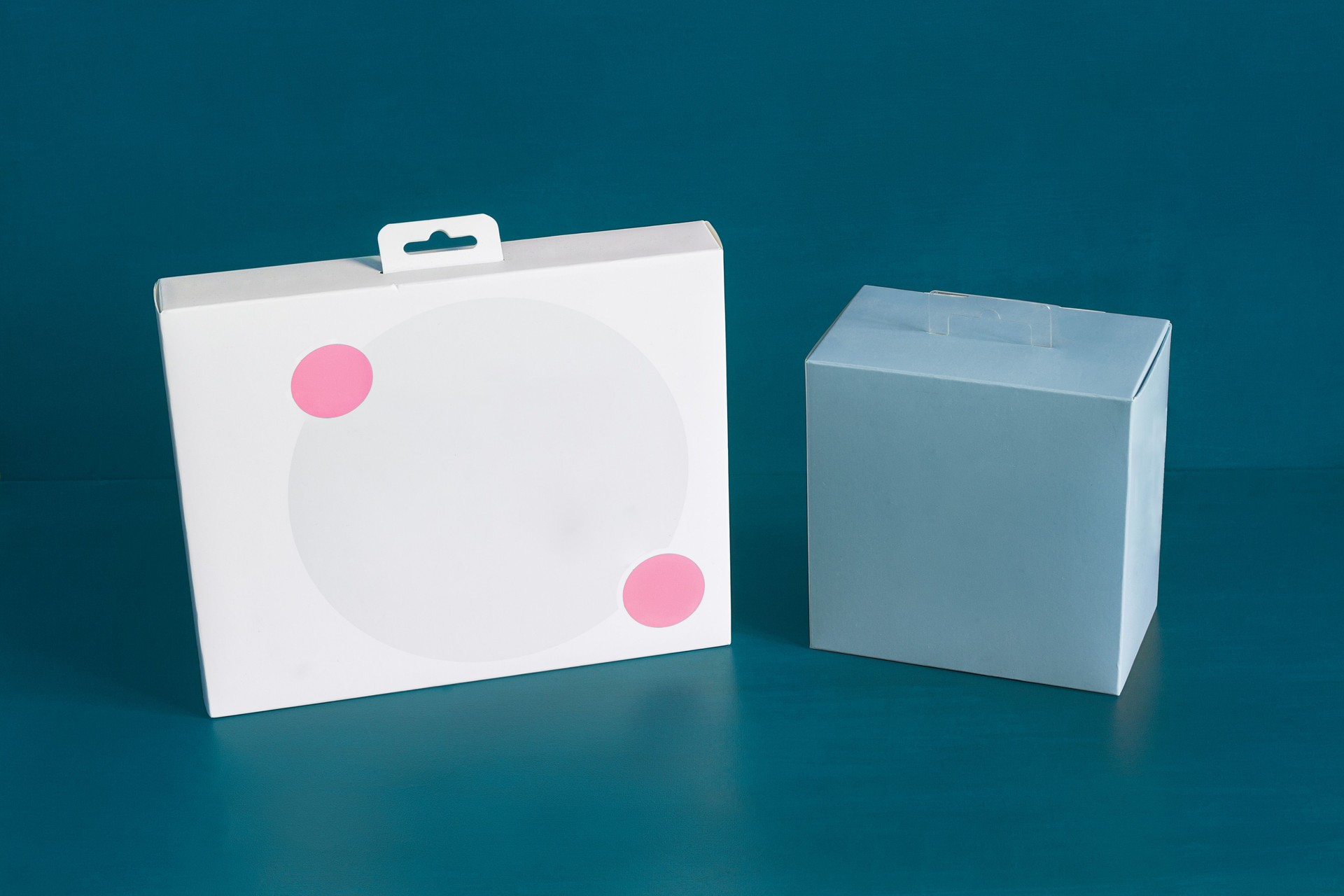 A white cardboard box with two decorative pink circles and a blank blue square box on a colorful blue studio background with copy space.